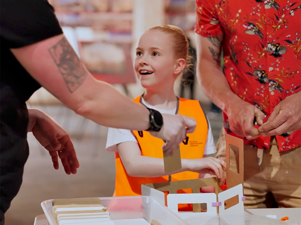 A girl in a hi-vis vest looks happy as she designs her own Footscray Hospital model