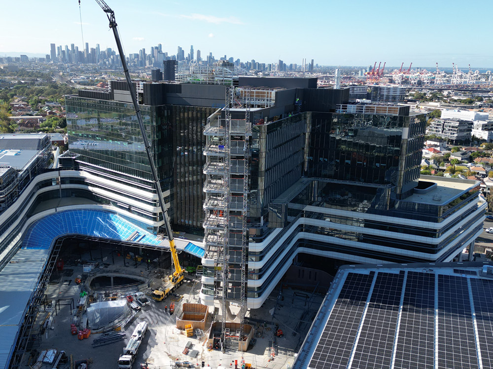 An aerial view of a tower of cladding beside the building, with a yellow and grey crane to its left 