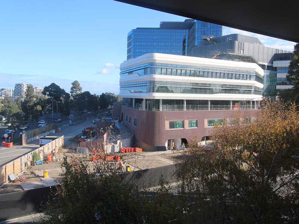 A construction site beside a building, contained within barriers that form a corner alongside two roads