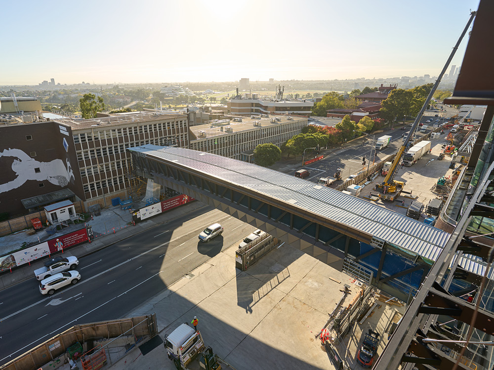 An aerial view of a roofed footbridge connecting two buildings over a road