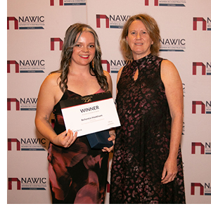 Two women stand proudly infront a NAWIC sign, holding an award that reads 'WINNER'