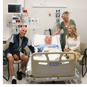 An older woman lying in a hospital bed surrounded by family looking happy and relaxed