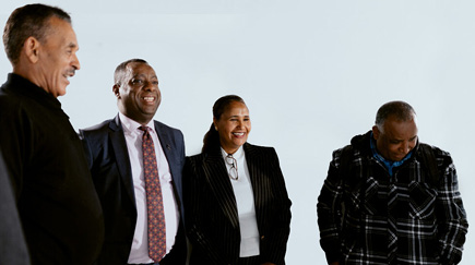 Three men and a woman standing against a white wall