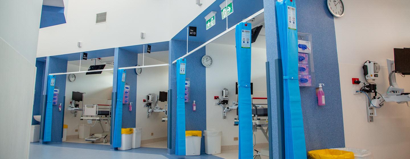 The interior of the Monash emergency department showing four cubicles in a row with blue walls and blue curtains