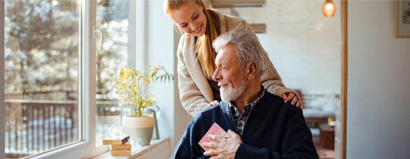 Stock image of elderly man sitting with a younger woman behind him smiling at the Numurkah aged care facility