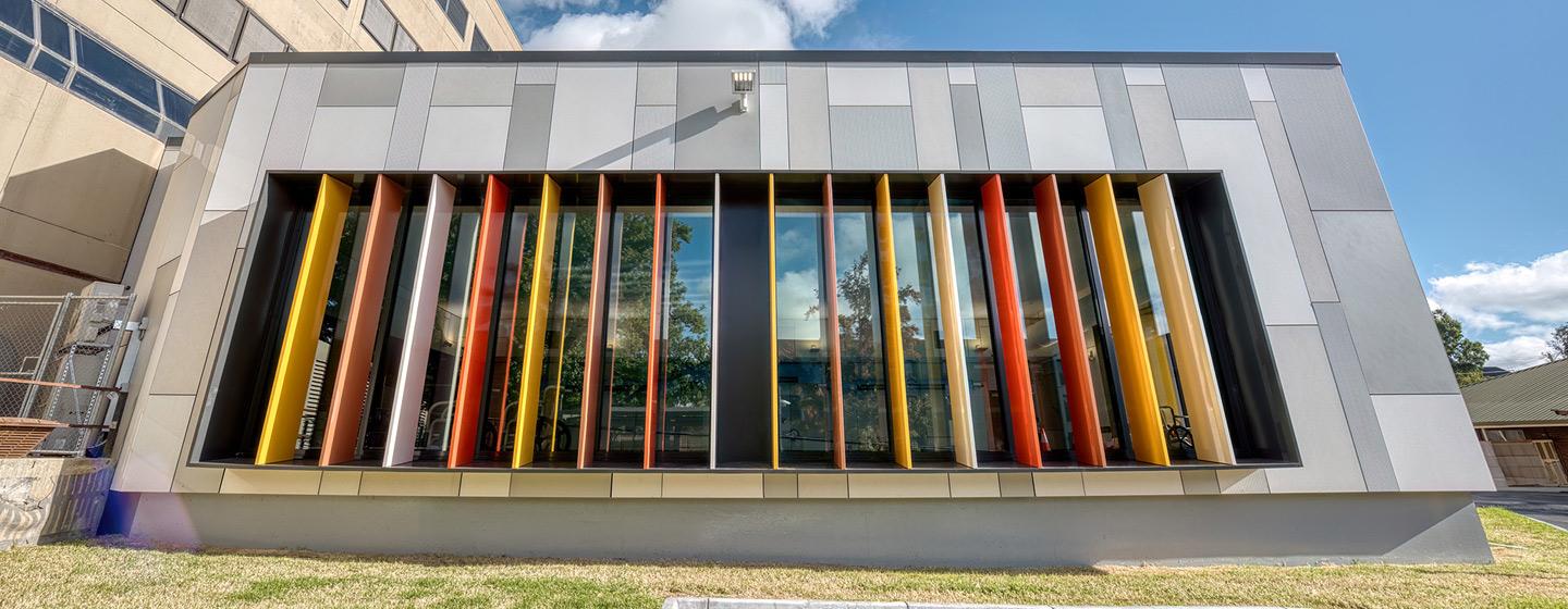 The exterior of Bendigo Hospital Day Rehabilitation Centre, with grey stone walls and multi coloured partitions across a large window