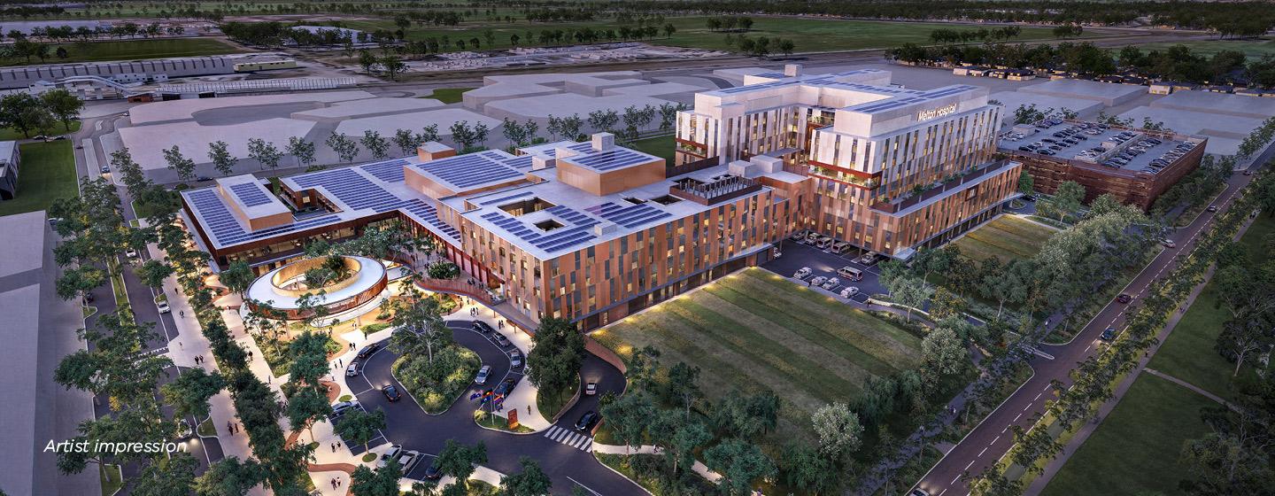 Artist impression of an aerial view of the exterior of the new Melton Hospital, seen in the evening with lighting turned on. Green space surrounds the buildings.