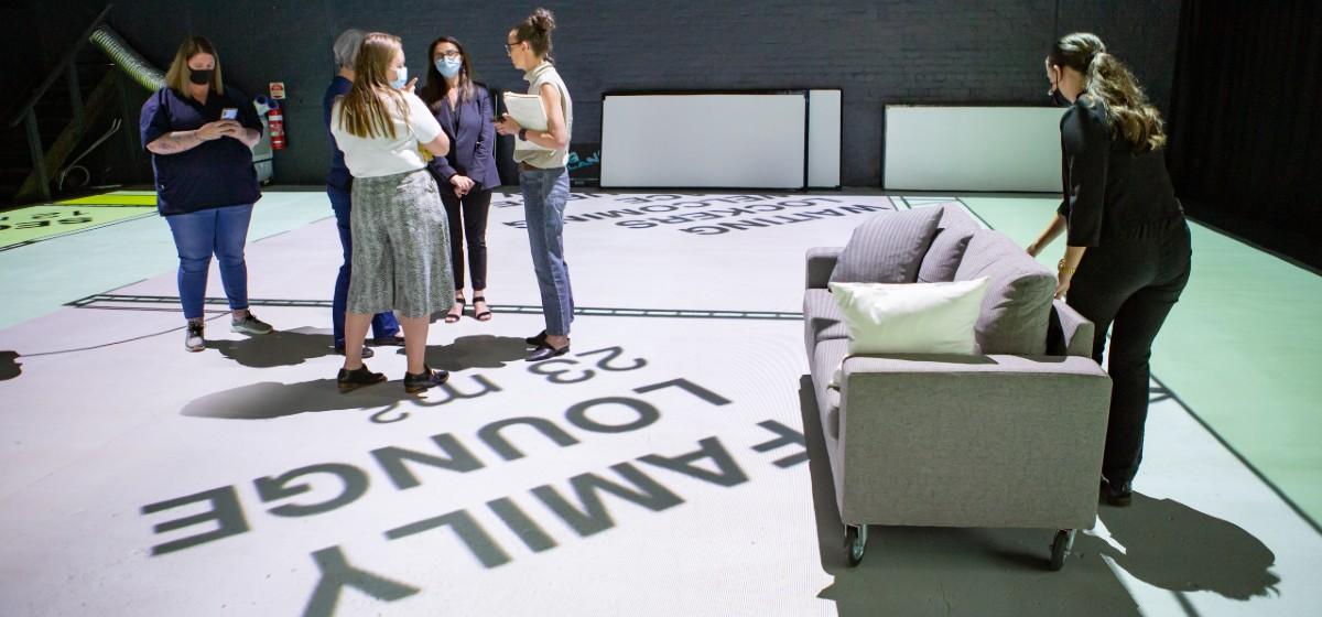 A small group of people stand in an open room with full-size projection of the proposed floor plan display of the floor..