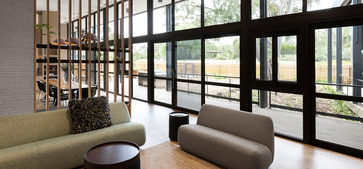 View of couches with floor-to-ceiling windows revealing a garden behind