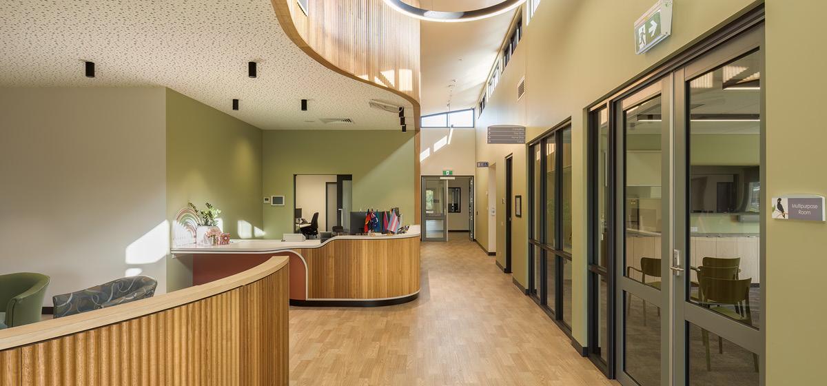 A reception area with timber floors, green walls, and further walling with organic curvature and timber finish