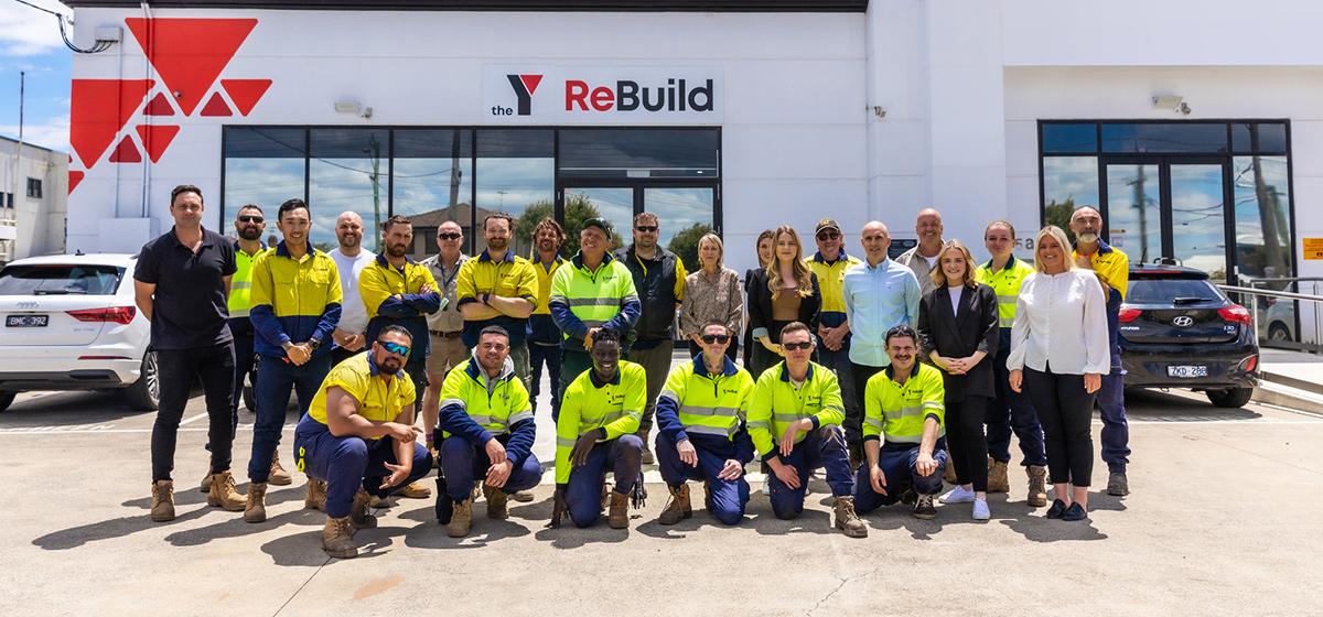 A large group of people in fluorescent vests pose for an photo in front of the YMCA ReBuild building