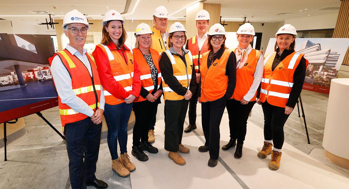 A group of men and women wearing hi-vis and white construction hats smiling proudly