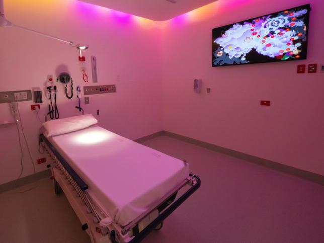 View Childrens’ Emergency Department Cubicle with television screen on wall, one bed/gurney and soft pink lighting