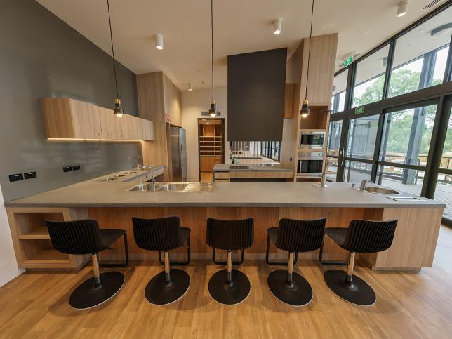 A modern kitchen with a row of black chairs by the benchtop