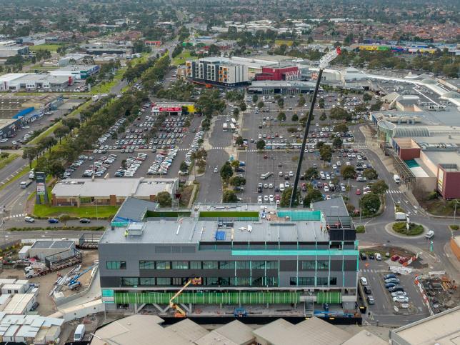 Aerial view of cranes installing a module on a hospital, with carpark behind