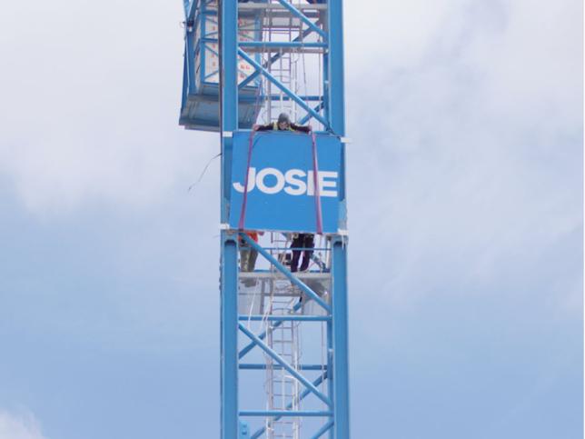 Close up aerial image of a construction worker placing the Josie sign on a crane at the Northern Hospital.