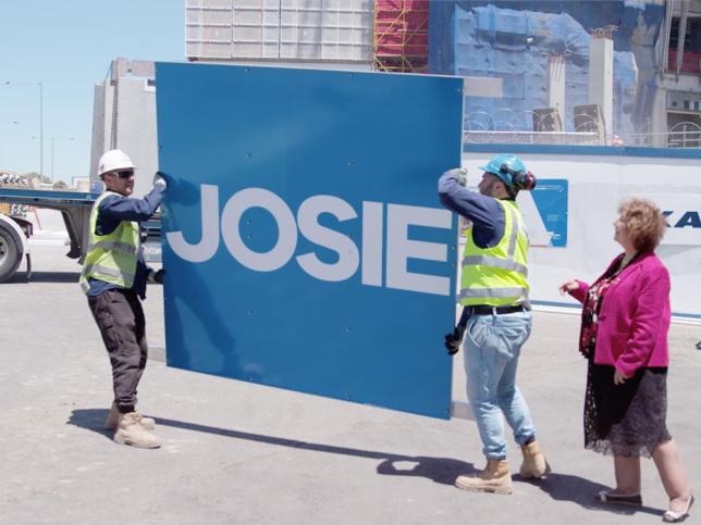 Construction workers carrying cladding that says 'Josie' while Josie Minniti stands next to them.