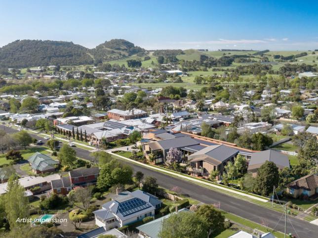 Aerial view of the Camperdown aged care facility. There is a long road in the middle, surrounded by building on either side. There is a hill with trees in the background.