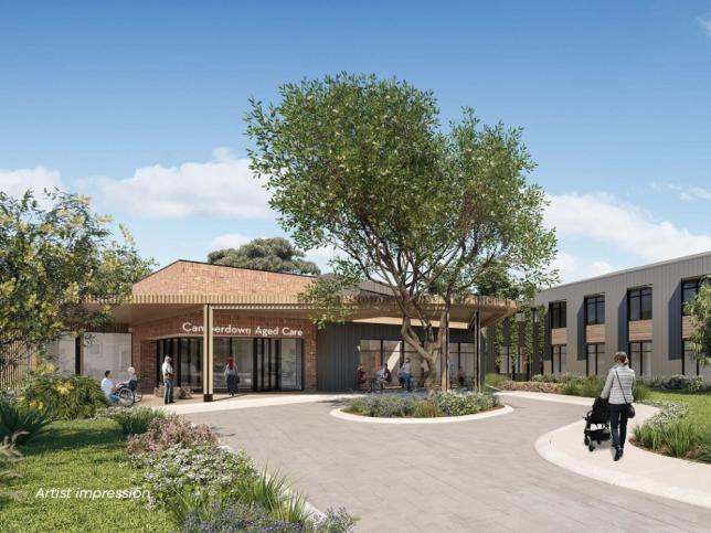 The outside of the Camperdown aged care facility. There is a large driveway and tree at the entrance. There are people walking.