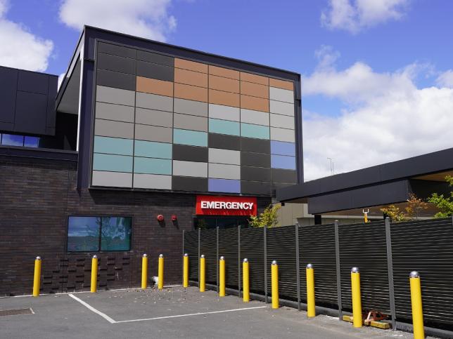 The entrance to the emergency area at Shepparton Hospital. The view is from the car park. There is a multi-storey glass building and a sign that reads 'EMERGENCY'