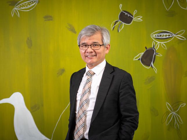 Dr Hai Buy standing in front of a green wall with a white bird and other animals painted.