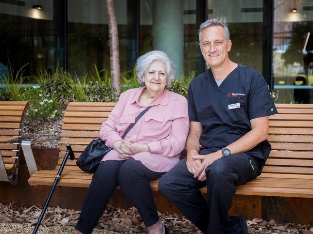 An elderly female Victorian Heart Hospital patients sits on a park bench with a clinician.