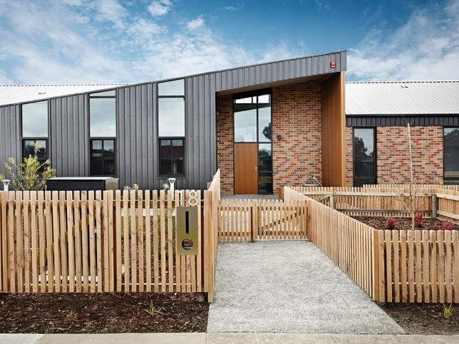 A view of the exterior of one of the areas housing mental health beds, with timber fences, and a brick and corrugated metal facade