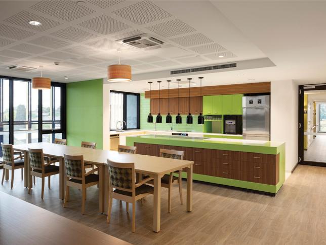 The kitchen and communal area at the St Georges aged care facility. The kitchen is green and thereis a long table with chairs in front of it.