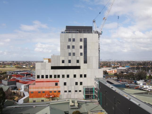 A view of the exterior of Joan Kirner Women's and Children's, with workers painting the lower left section in orange and red