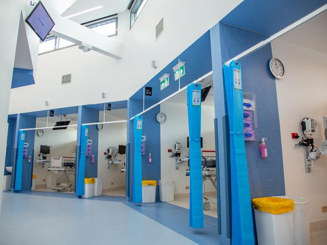 A row of cubicles inside an emergency department, with blue walls and blue curtains