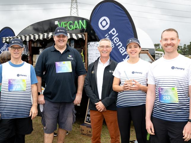 Five people in active wear branded with the Plenary Health logo stand smiling at the camera