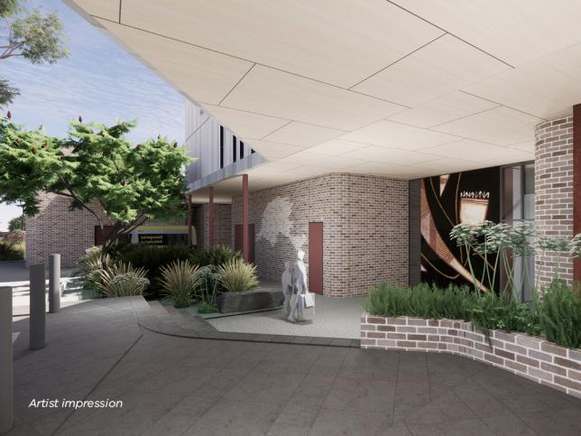 Artist impression of the main entry of the Phillip Island Community Hospital. The entry has a verandah for weather protection and features native plants to soften the grey brickwork, first nations artwork and a map of Phillip Island is inlaid in the bricks