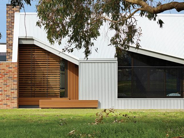 The back of a building, with a corrugated metal exterior and a section of timber panels partially covering a window