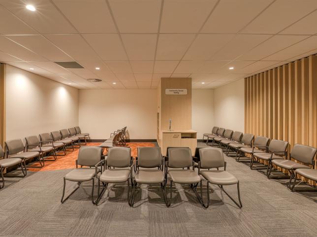 A waiting area with white walls lined with timber slats, a brown floor, and many brown chairs in rows