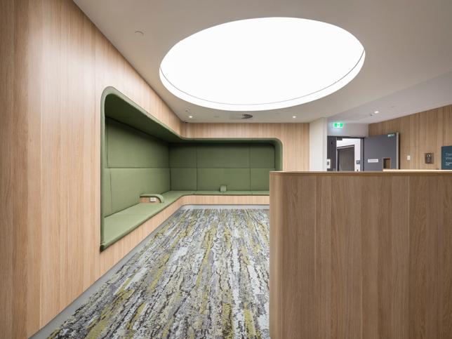 Green alcove seating in a timber wall, with carpeted floors and a fluorescent white light in the ceiling