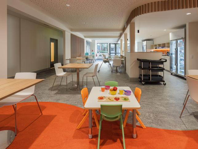 Communal dining area with orange carpet and colourful chairs.