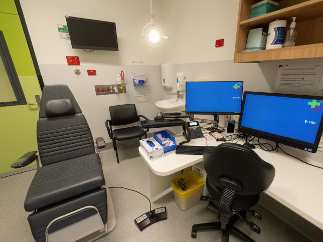 A consultation room with a patient chair, desk and screens