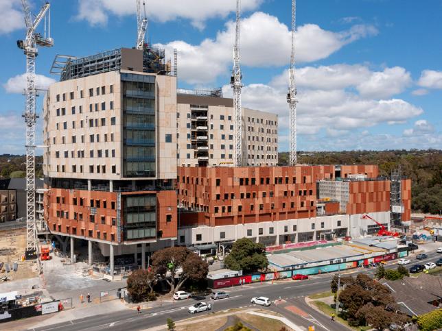 A view of the hospital against blue skies and clouds with cranes stretching upwards along the skyline