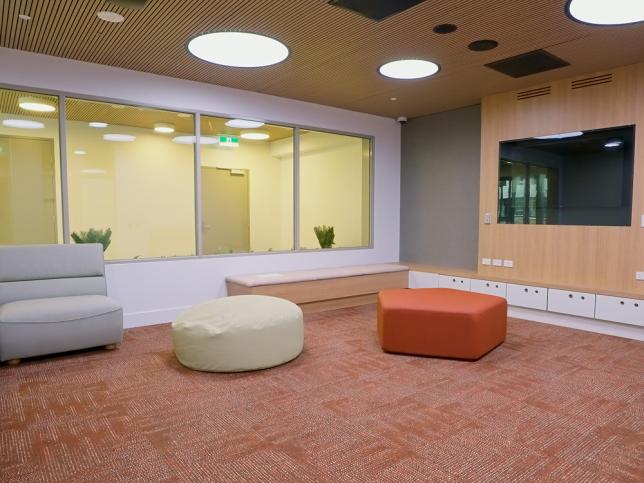 A brightly-lit room with carpet floors, stools, couches and timber walls and ceiling