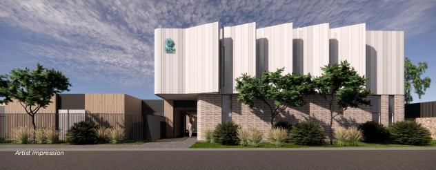 Artist impression of the Northern facade of the Phillip Island Community Hospital. The hospital will be two stories high and the outside is a sandy coastal color. There are native plants surrounding the building.