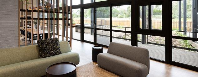 Couches in a living room with floor to ceiling windows showing garden behind