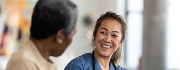 A female medical staff member wearing scrubs smiling at a male patient.