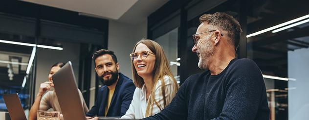 Four people sitting at a table in an office, laughing and smiling.