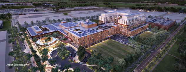 Artist impression of an aerial view of the exterior of the new Melton Hospital, seen in the evening with lighting turned on. Green space surrounds the buildings.