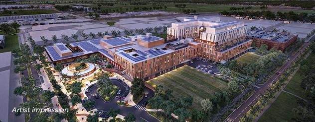 Artist impression of an aerial view of the exterior of the new Melton Hospital, seen in the evening with lighting turned on. Green space surrounds the buildings