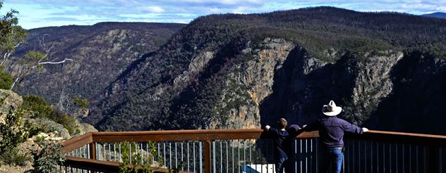 Adult and child at lookout gaze out at expansive mountain ranges 